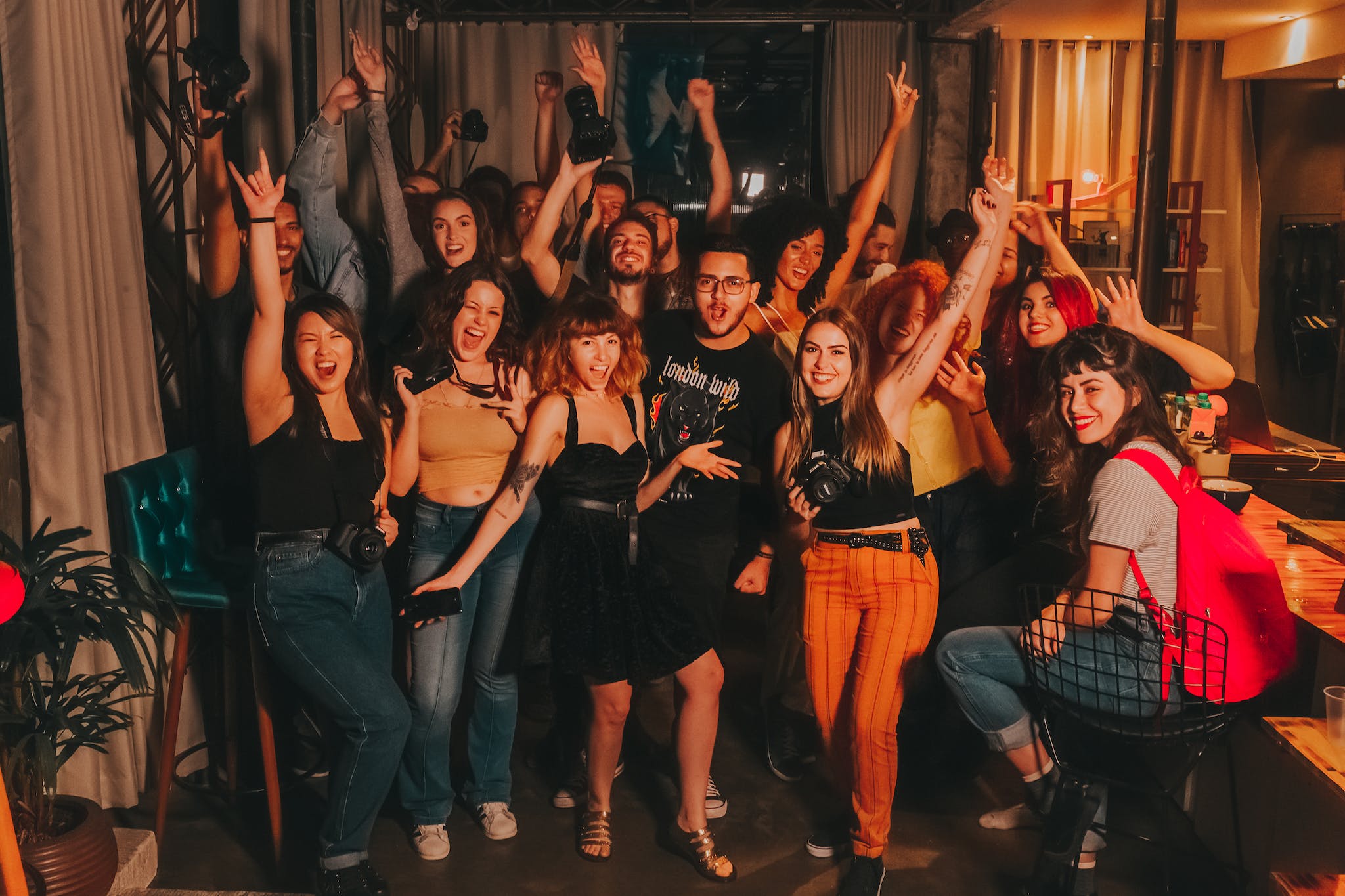 High angle of excited young diverse friends in casual outfits with arms raised yelling happily while celebrating project success in modern workspace